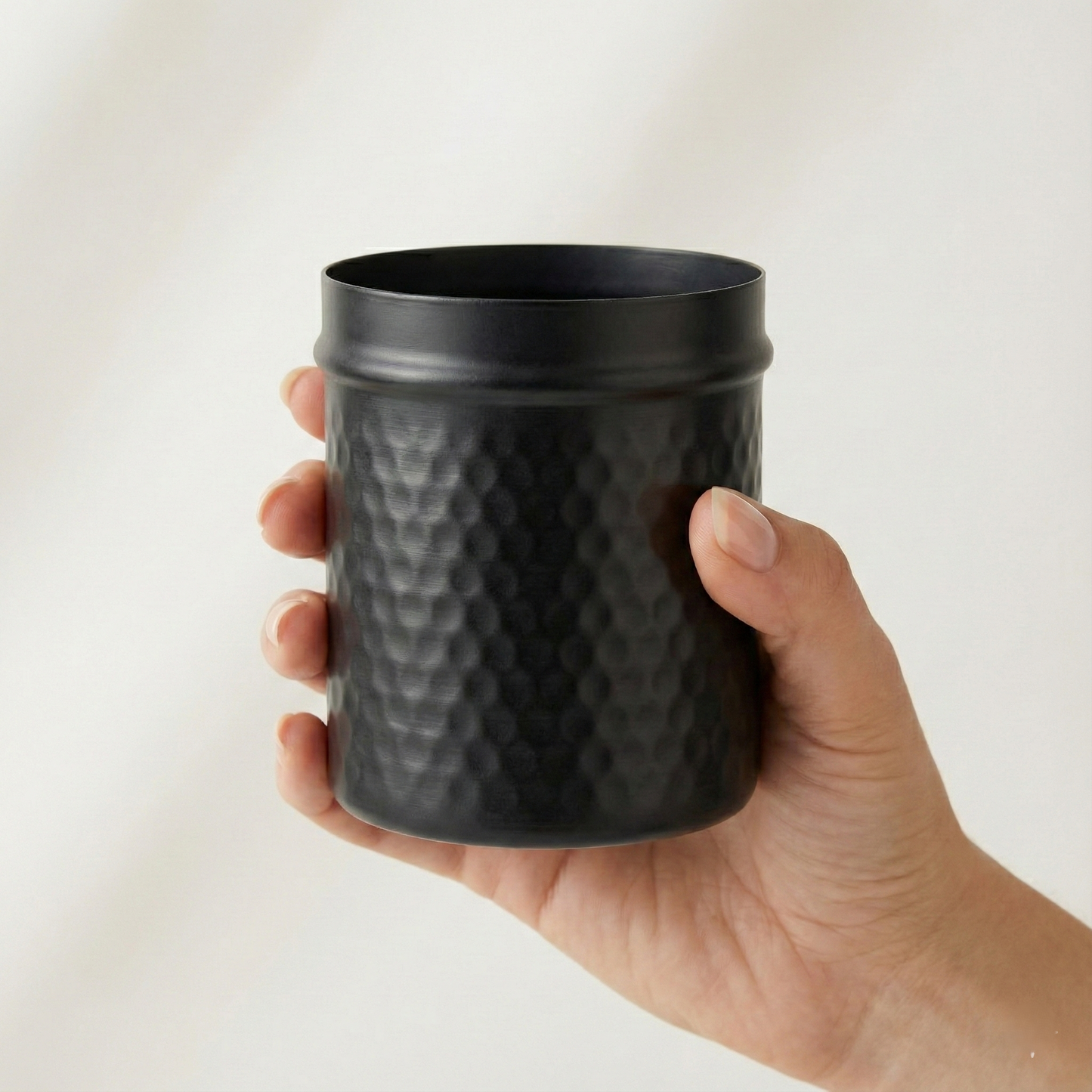 Hand holding PreYog Matte Black Iron Jar to show 4-inch scale. Compact hammered metal container size reference.
